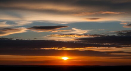 Obraz premium Vibrant sunset paints the sky with orange gold and blue clouds over a dark horizon