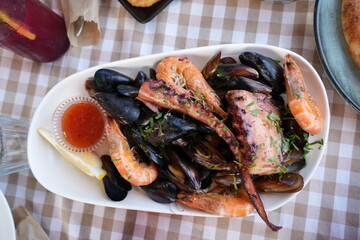 Seafood platter with shrimp, mussels, and octopus served in a restaurant. Fresh Mediterranean cuisine with grilled seafood and herbs on a checkered tablecloth.