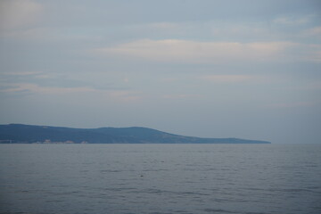 Calm seascape with distant mountains on the horizon under a soft cloudy sky. Minimalistic coastal view with gentle tones, perfect for themes of nature, travel, serenity, and peaceful landscapes.