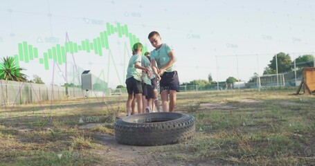 Straining six children pulling rope on tractor tire at school playground, with chain link fence