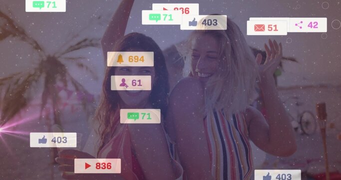 Posing friends wearing swimsuits on beach at sunset, showing smartphone with social notifications