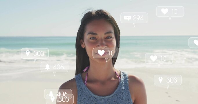 Standing woman wearing blue crochet top over pink bikini on beach, with floating social media icons