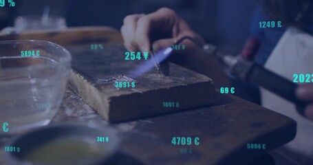 Heating metal with torch on firebrick at workbench wearing protective apron with currency symbols