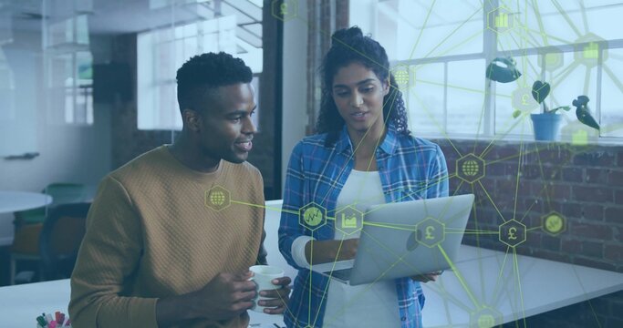 Colleagues collaborating on laptop at high desk in office, with network icons overlay, coffee mug - Powered by Adobe