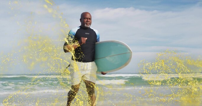 Striding Black man wearing rash guard on beach holding turquoise surfboard with golden sparkles