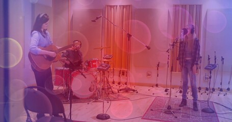 Three musicians recording song in studio, wearing headphones with acoustic guitar and red drum kit