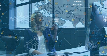 Analyst wearing blazer manipulating world map overlay at office desk, using stylus and smartphone