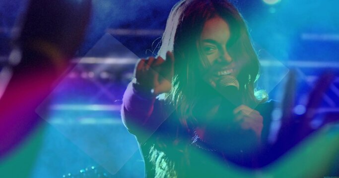 Female singer singing and pointing on center stage under vibrant lighting, with microphone and haze