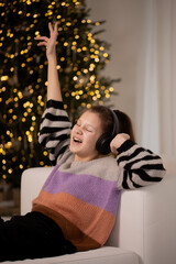 Teen girl singing with headphones near glowing Christmas tree