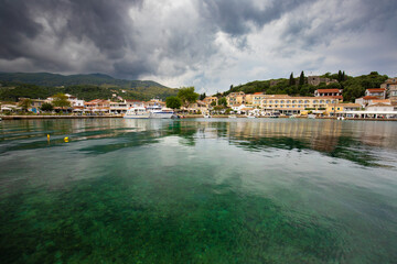 Obraz premium The picturesque harbor of Kassiopi, a charming fishing village located on the northeastern coast of the Greek island of Corfu, background or wallpaper for the project
