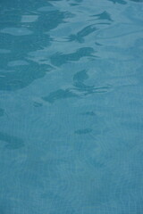 Blue swimming pool water surface with gentle ripples and sunlight reflections. Calm aqua texture creating a refreshing and relaxing summer atmosphere. Perfect background for vacation, spa, and wellnes
