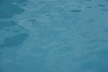 Blue swimming pool water surface with gentle ripples and sunlight reflections. Calm aqua texture creating a refreshing and relaxing summer atmosphere. Perfect background for vacation, spa, and wellnes