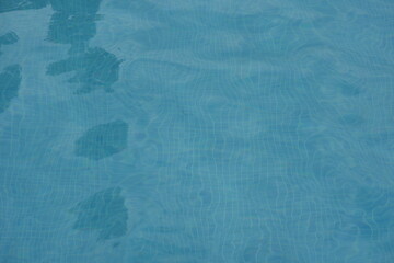 Blue swimming pool water surface with gentle ripples and sunlight reflections. Calm aqua texture creating a refreshing and relaxing summer atmosphere. Perfect background for vacation, spa, and wellnes