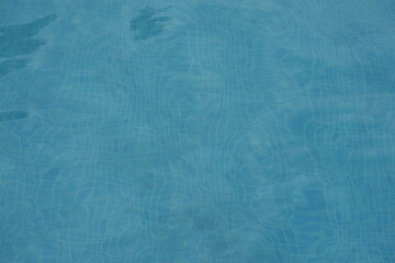 Blue swimming pool water surface with gentle ripples and sunlight reflections. Calm aqua texture creating a refreshing and relaxing summer atmosphere. Perfect background for vacation, spa, and wellnes