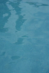 Blue swimming pool water surface with gentle ripples and sunlight reflections. Calm aqua texture creating a refreshing and relaxing summer atmosphere. Perfect background for vacation, spa, and wellnes
