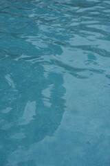Blue swimming pool water surface with gentle ripples and sunlight reflections. Calm aqua texture creating a refreshing and relaxing summer atmosphere. Perfect background for vacation, spa, and wellnes