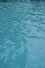 Blue swimming pool water surface with gentle ripples and sunlight reflections. Calm aqua texture creating a refreshing and relaxing summer atmosphere. Perfect background for vacation, spa, and wellnes