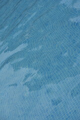 Blue swimming pool water surface with gentle ripples and sunlight reflections. Calm aqua texture creating a refreshing and relaxing summer atmosphere. Perfect background for vacation, spa, and wellnes