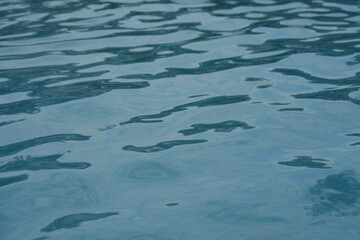 Blue swimming pool water surface with gentle ripples and sunlight reflections. Calm aqua texture creating a refreshing and relaxing summer atmosphere. Perfect background for vacation, spa, and wellnes