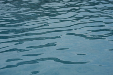 Blue swimming pool water surface with gentle ripples and sunlight reflections. Calm aqua texture creating a refreshing and relaxing summer atmosphere. Perfect background for vacation, spa, and wellnes