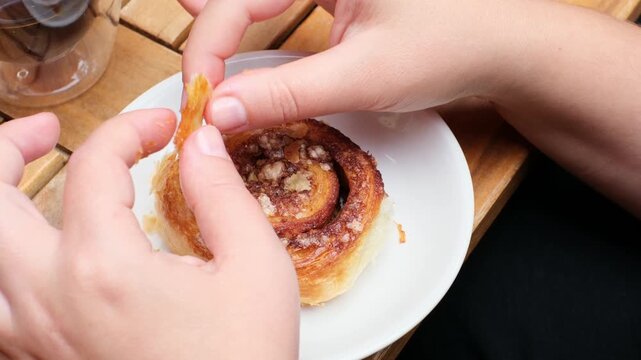 Hands delicately pulling apart a cinnamon roll on a cozy wooden table, showcasing the warm, flaky texture and inviting aroma of autumn treats during a friendly gathering