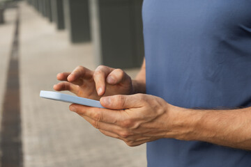 Man wearing blue t-shirt using and texting mobile phone. Check apps, focused on device, chatting or browsing internet. Outdoors.