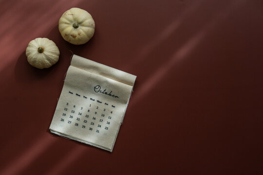 Top view of linen fabric calendar with October month, decorative pumpkins, brown background, minimal aesthetic