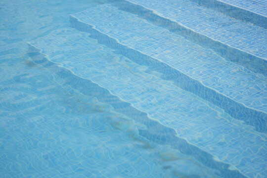 Clear blue swimming pool with underwater steps. Calm, clean water surface and light reflections creating a refreshing summer atmosphere. Perfect for themes of vacation, wellness and relaxation. - Powered by Adobe