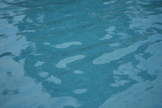 Blue swimming pool water surface with gentle ripples and sunlight reflections. Calm aqua texture creating a refreshing and relaxing summer atmosphere. Perfect background for vacation, spa, and wellnes