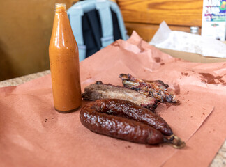 Texas BBQ smoked beef brisket and sausage with homemade sauce bottle on pink butcher paper at Luling City Market barbecue restaurant