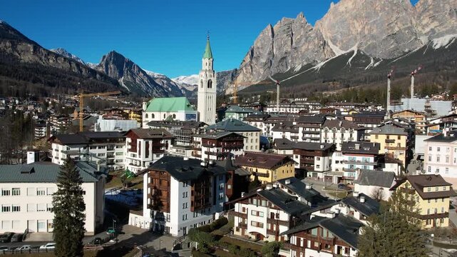 Aerial Reveal of Cortina d'Ampezzo from the Central Church to Dolomites Mountain Range: 4K Drone View of 2026 Winter Olympic Games Host City, Snowy Alpine Townscape and Ski Resort Venue, Italy