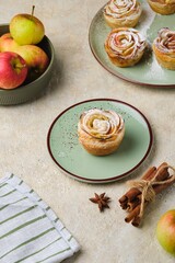 Puff pastry with rose-shaped apples dusted with powdered sugar on a green ceramic plate against a light concrete background.