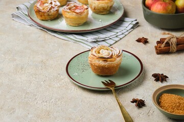 Puff pastry with rose-shaped apples dusted with powdered sugar on a green ceramic plate against a light concrete background.