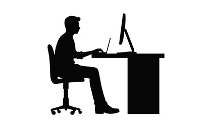 Young man working at a desk using a computer in silhouette  