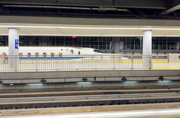 Shinkansen bullet train at station platform, Japan. Glass safety barriers, yellow tactile paving,