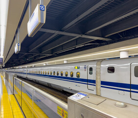 Shinkansen bullet train at station platform, Japan. Glass safety barriers, yellow tactile paving,