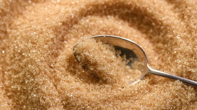 Brown Cane sugar in a spoon close up. Brown sugar background. Heathy eating, diet concept. Top view, flat lay, slow motion, rotating 