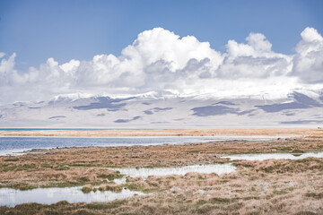 Panorama landscape of Lake Karakul in the Pamir mountains in the Tien Shan against the background of high snowy rocky peaks with clouds, morning panorama of the lake for the background