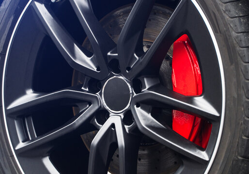 Black matte cast disc with a red caliper. The car wheel with a red caliper, pads, brake disc. Car showroom. Car alloy wheel and tyre close-up. Car Braking System - Close-Up of SUV Front Wheel Brake