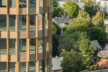 Modern residential or office building with golden facade and glass windows overlooking green trees and suburban houses in the city of Vilnius