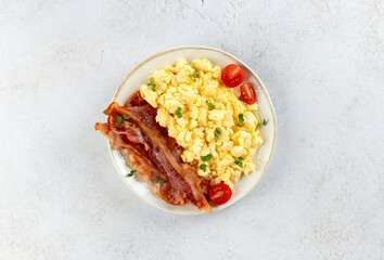 Scrambled eggs with crispy bacon and tomatoes on a white background. Classic breakfast.
