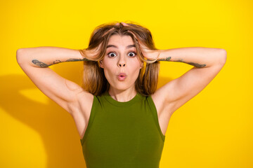 Fototapeta premium Excited young woman expressing surprise with hands on her head against a vibrant yellow background