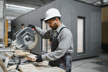 Carpenter cutting wood with circular saw in prefabricated house workshop