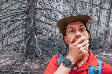 A shocked hiker in the forest covers his mouth with fear representing concepts of wilderness...