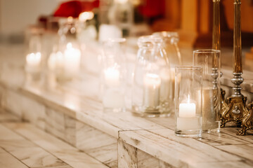 Romantic wedding church decoration with burning candles in glass holders and floral arrangements, warm light creating peaceful atmosphere for ceremony and celebration
