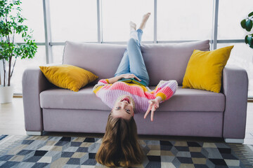 Young woman enjoying leisure time upside-down on a cozy couch with a cheerful pose in a stylish indoor setting