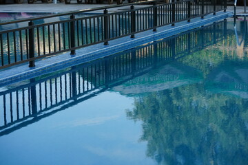 Elegant reflection of a modern poolside fence in calm blue water — symbol of balance, clarity, and relaxation. Perfect for hotel marketing, travel brochures, wellness brands, and real estate visuals. 