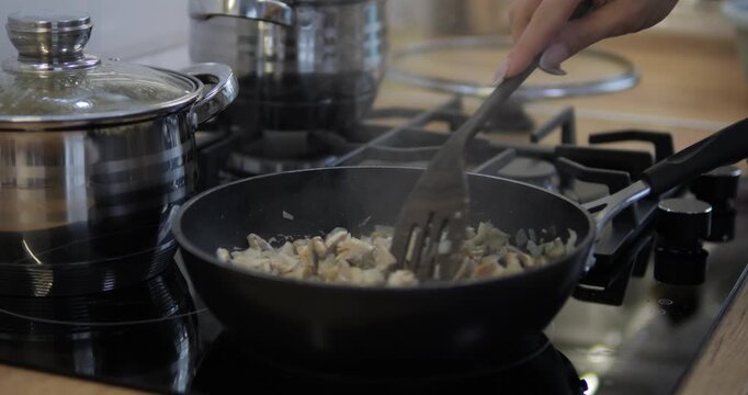 The hostess is preparing a dish with mushrooms and pasta in the kitchen. A stove with a frying pan and pots.