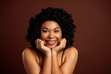 Naklejka premium Beautiful young woman with a confident smile and natural curly hair posing against a brown background, embracing elegance