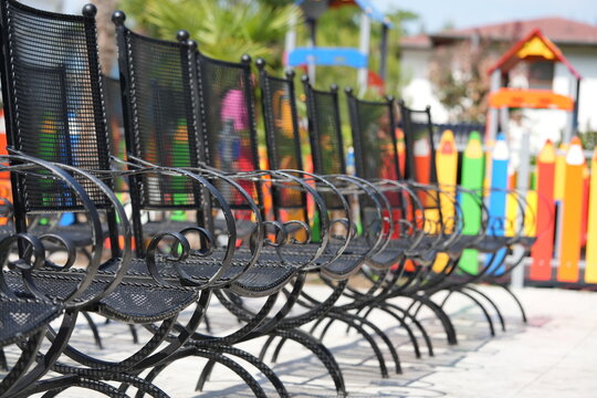 Metal outdoor chairs arranged in rows at a sunny street café. Urban seating area with black and colorful chairs, creating a modern geometric pattern.